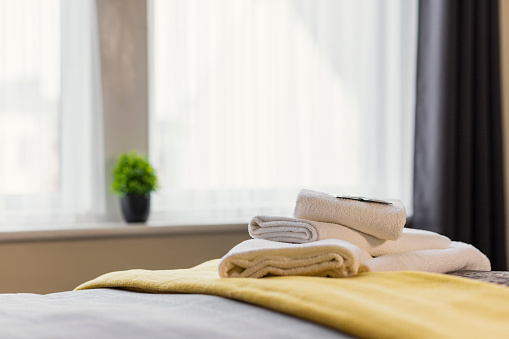 A hotel bedroom in Whitley Bay, North East England. The main focus is towels folded and organised neatly on the bed with shampoo and conditioner sachets on them. The window is in the background of the shot.