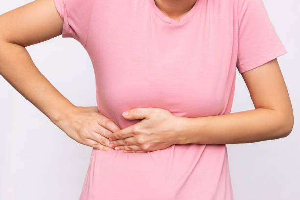 A young woman holding her side with her hands. Sore side under the rib after training. Stomach pain Cropped shot of a young woman in a pink t-shirt holding her side with her hands isolated on a white background. Sore side under the rib after training. Stomach pain female rib cage stock pictures, royalty-free photos & images