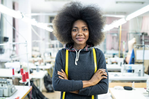 Portrait of a happy smiling african american woman designer as a startup business owner standing with arms crossed in her tailor studio and looking at the camera Happy smiling african american woman designer as a startup business owner working in her tailor studio woman tailor stock pictures, royalty-free photos & images