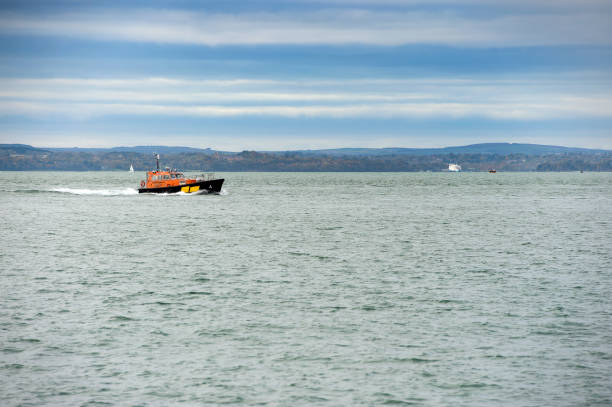 Egmond aan Zee, Netherlands - May 13, 2023: A Dutch coast guard rescue boat (Reddingsbrigade KNRM) speeds through choppy waters, leaving a white foam trail behind. Crew members are actively engaged, dressed in safety gear as they patrol the coastline under bright sunlight