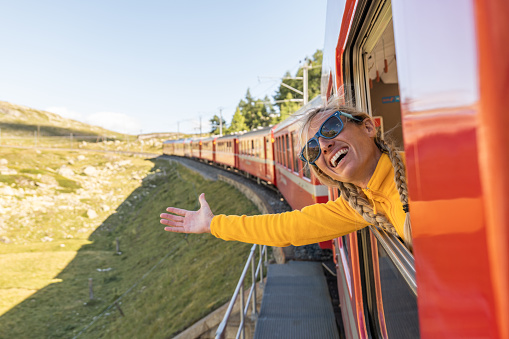 Joyful woman enjoying train ride in Switzerland, arms outstretched