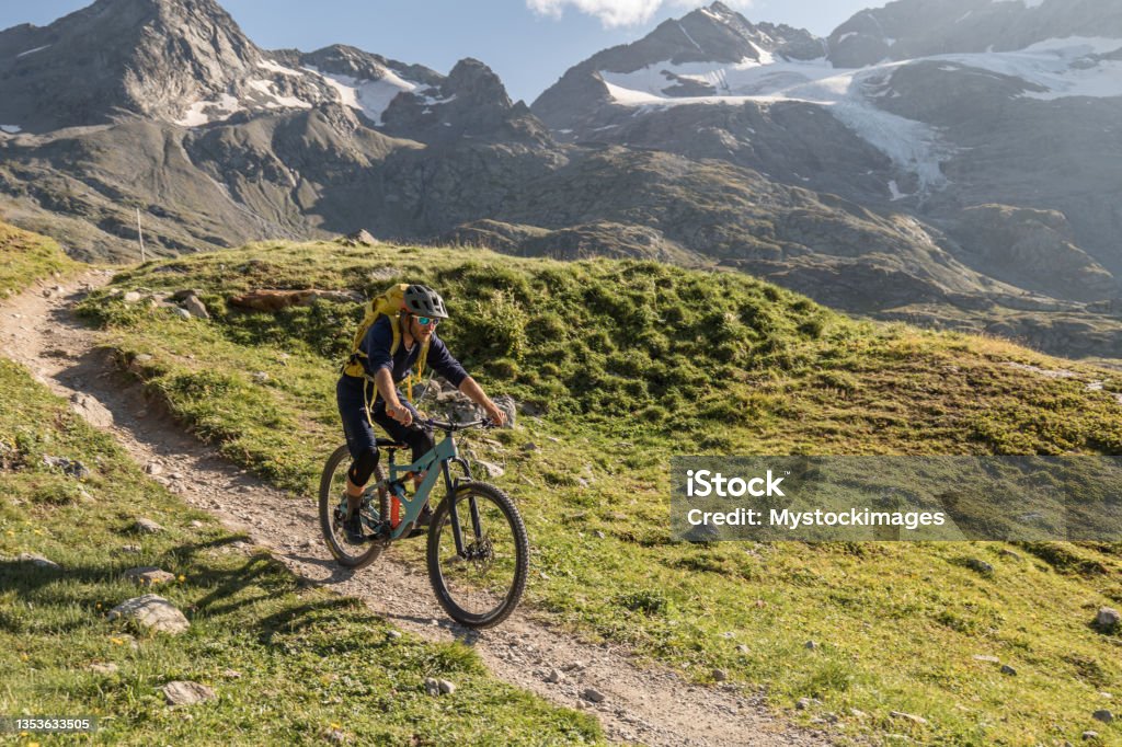 Mountain biker rides along alpine lake He flows on a dirt bike trail and enjoys nature at sunset Biker Stock Photo