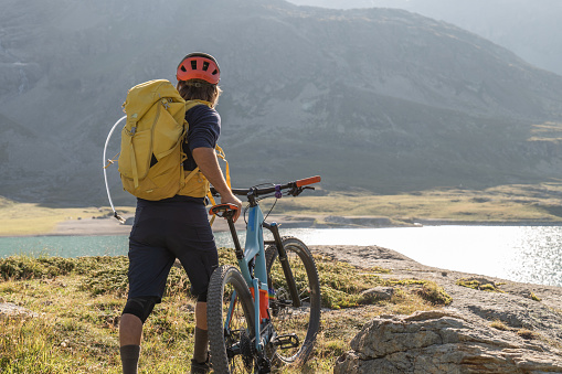 He stops on a rock above a glacier lake at sunset and enjoys the panorama. Graubunden canton, Switzerland