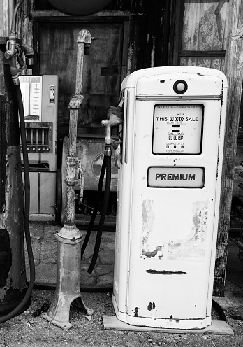 Beautiful black woman pouring gas into her car and using smart phone at the gas station.