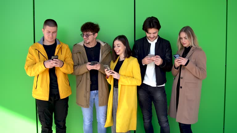 Diverse people guys and girls sitting together holding mobile phones, feel more comfortable chatting online than talking real life. Generation addicted to their smartphones modern technologies concept