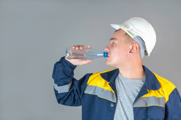istock A construction worker in a white helmet and work clothes drinks water from a plastic bottle 1353640666