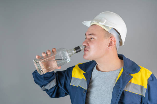 istock Aggressive worker in a hard hat drinks strong alcohol from a glass bottle, close-up 1353640669