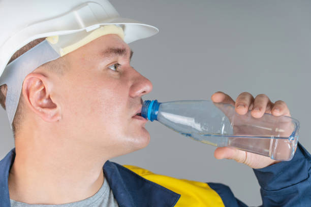 istock A construction worker in a white helmet and work clothes drinks water from a plastic bottle, close up foto 1353640672