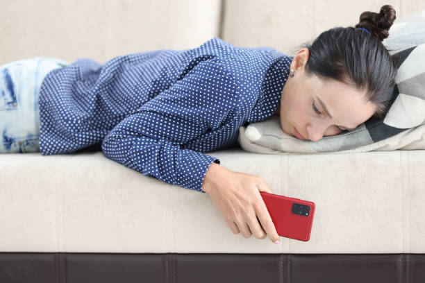悲しい女性はスマートフォンのクローズアップでソファに横たわっている - lying in wait ストックフォトと画像