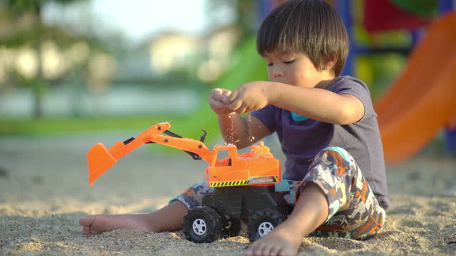 Little boy playing the sand with an Excavator toy at the playground alone
