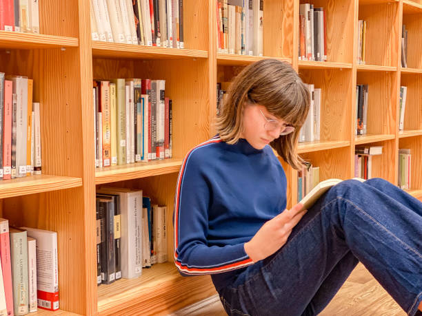 istock Young teenager reading a book in the library 1353649855