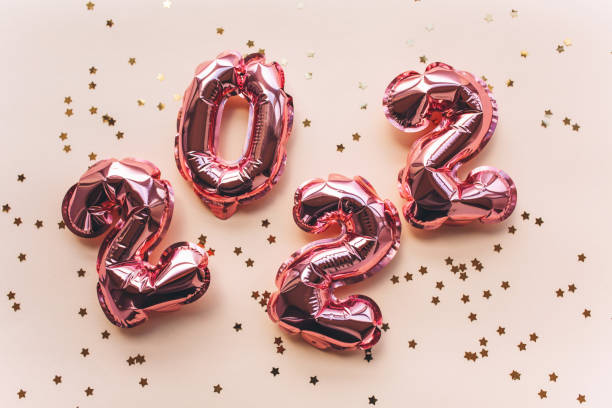 Balloons made of pink foil in the form of numbers 2022 with confetti on a pink background . Celebrating Christmas, New Year and festive concept. Flat lay, top view. stock photo