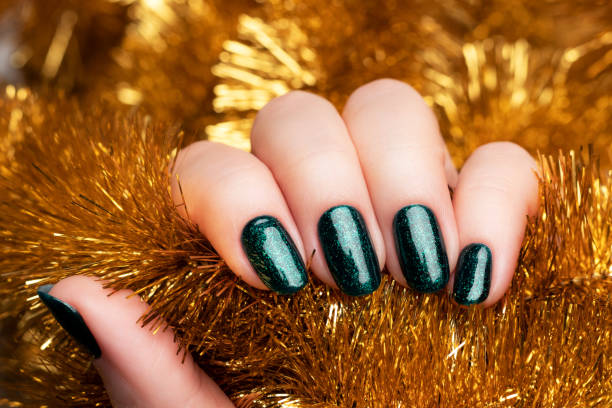 istock Hand with green glittered nails with golden tinsel 1353652798