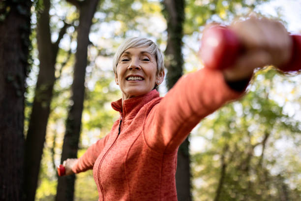 istock Active senior woman lifting dumbbells with arms outstretched looking at camera 1353652800