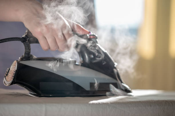 Iron with steam and water stream close-up. Ironing clothes on ironing board. stock photo