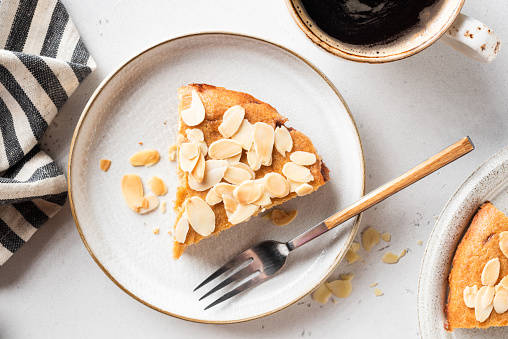 Portion of almond cake on dessert plate served with cup of black coffee, closeup top view