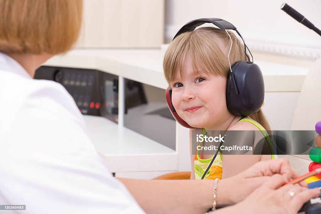 Female audiologist testing a young girls hearing Doctor audiologist testing girl's ears on medical equipment Child Stock Photo