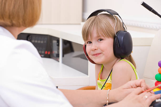 Female audiologist testing a young girls hearing Doctor audiologist testing girl's ears on medical equipment girl flex stock pictures, royalty-free photos & images