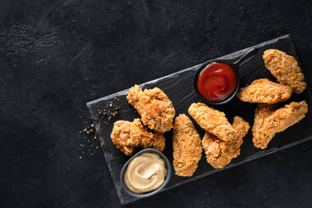 Crispy fried chicken wings with sauces Crispy fried chicken wings with sauces served on black slate board, top view, copy space. Junk food nuggets heat stock pictures, royalty-free photos & images