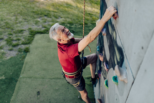 Senior man climbing on the artificial rock and having fun.