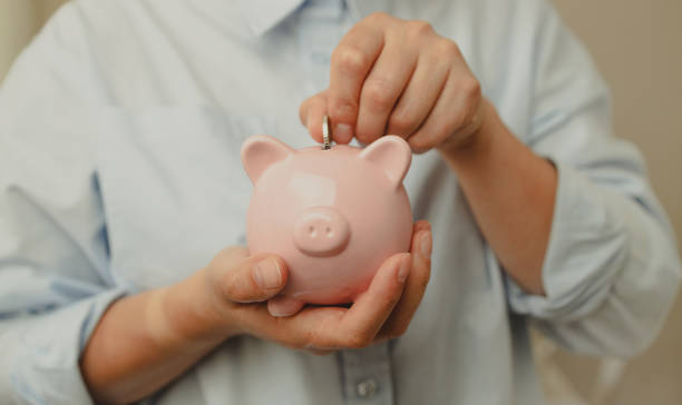 Depositing money in a piggy bank on wooden table at home. Saving money for future plan and retirement fund concept stock photo