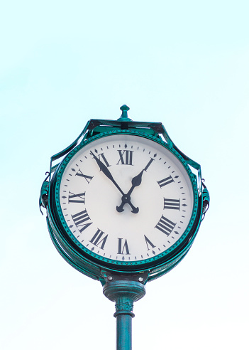 Green city clock on blue sky background. Vertical photo