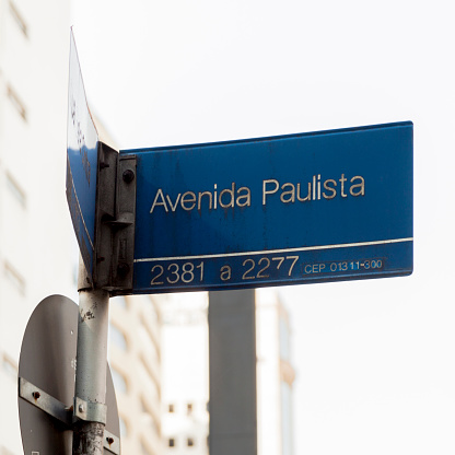 Paulista Avenue sign with mirrored buildings in the background during the day. Sign with usage, age and pollution marks. São Paulo avenue concept. Concept of São Paulo.