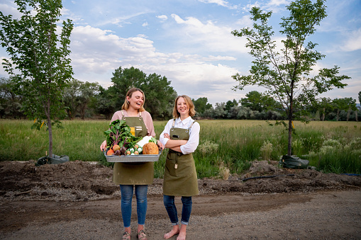 Two Happy Young Women Standing In A Field  Proudly Displaying Produce Grown On Their Farm