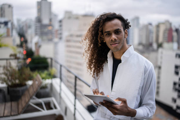 Portrait of a young man holding a digital tablet on a rooftop Portrait of a young man holding a digital tablet on a rooftop gay long hair stock pictures, royalty-free photos & images