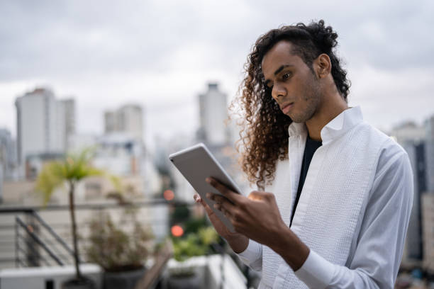 Young man using a digital tablet on a rooftop Young man using a digital tablet on a rooftop gay long hair stock pictures, royalty-free photos & images
