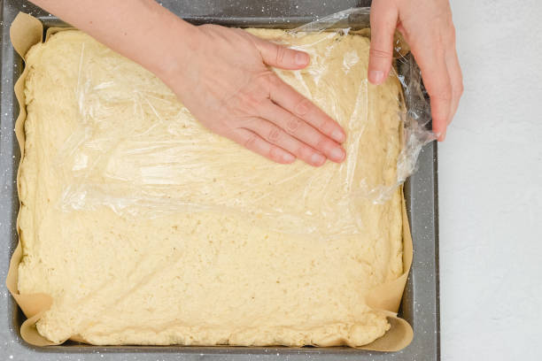 istock Woman's hands using plastic wrap unfurl pizza dough onto prepared baking pan. Close up baking process, flat lay 1353664191