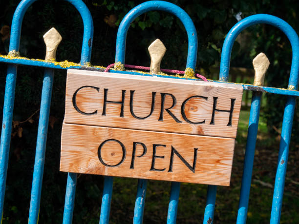 A wooden sign hanging on a blue painted church gate reading “Church Open” in black-painted and incised capital letters.
