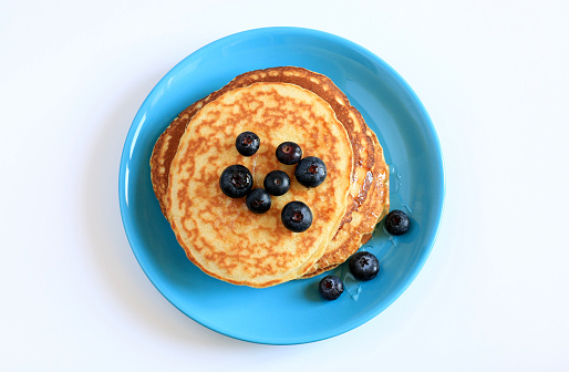 Stack of homemade pancakes on turquoise blue plate with blueberries on white background. Directly above.
