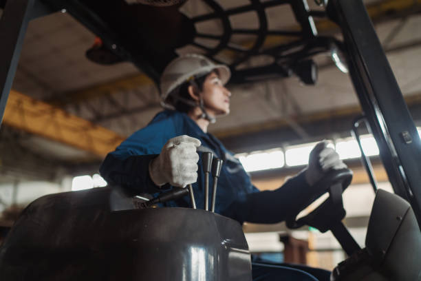 construction industry - female asian skilled labour worker driving a forklift in reverse - empilhadora imagens e fotografias de stock