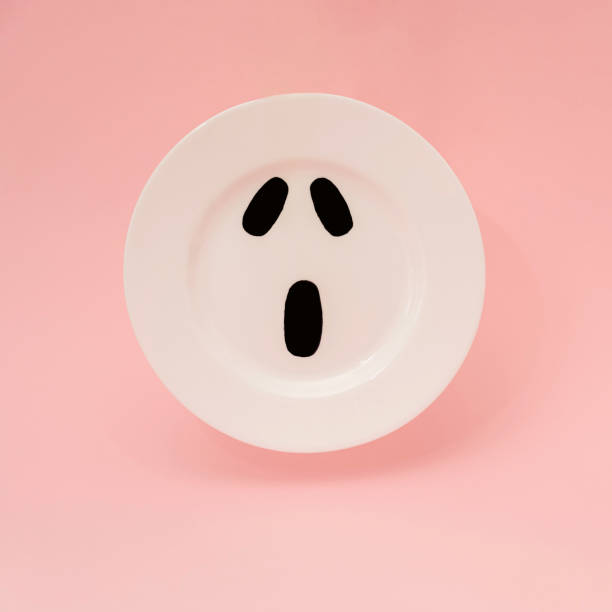 istock Scary face on a white plate floating against light pink background. Minimalist Halloween concept. 1353669476