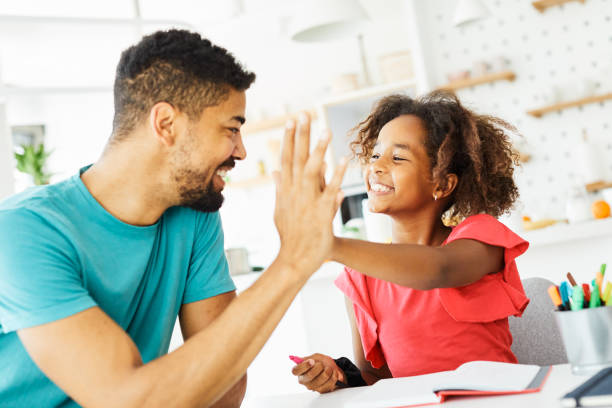 compiti a casa che insegnano alto cinque educazione padre figli figlia famiglia infanzia successo bambino afroamericano - hometeam foto e immagini stock