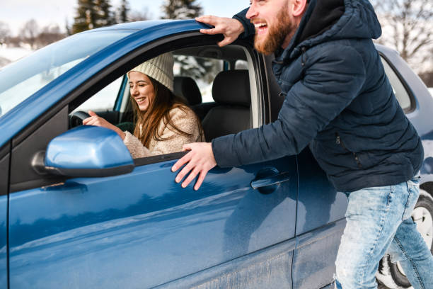 istock Smiling Female Having Boyfriend Push Car While Stuck In Snow 1353675761