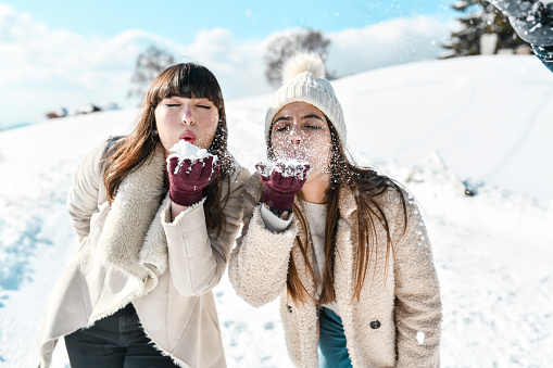 Two Cute Females Blowing Fresh Snow On Mountain