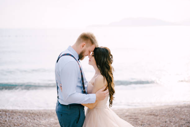The bride and groom stand on the pebbled seashore and hug