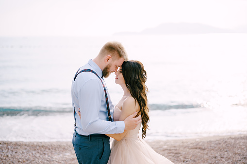 The bride and groom stand on the pebbled seashore and hug . High quality photo