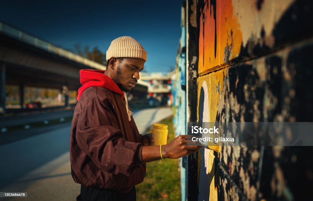 Street artist drawing graffiti on the wall. Closeup side view of a young African American man creating street art drawing on the wall. Graffiti Stock Photo