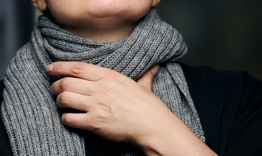 a gray scarf is wrapped around the neck, and a hand is holding the throat. Cold and sore throat