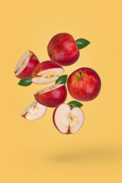 istock Minimal fruit concept with fresh sliced and whole apple floating in the air isolated on yellow background. 1353691739