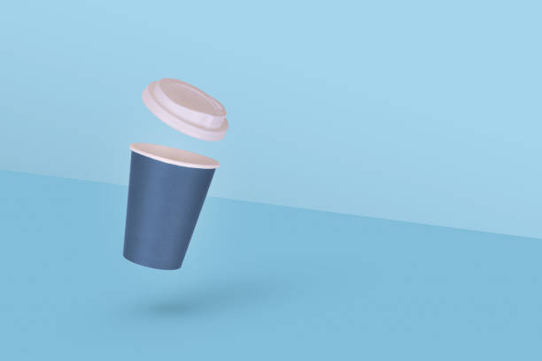 istock One disposable paper coffee cup with white cap flying in air isolated on blue background. 1353691743