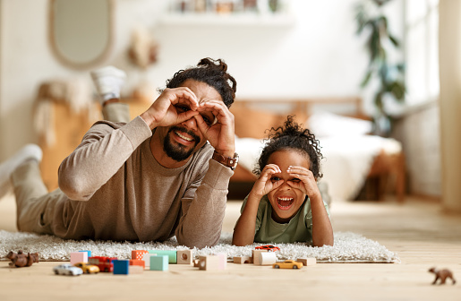 Happy african american family father with little son playing together, making binoculars with hands