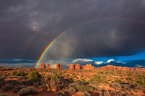 Dramatic, stormy sky with sunlight and a double rainbow over Balanced Rock in Arches National Park, Utah, USA.