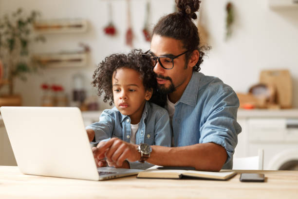 istock Young african american dad helping schoolboy son with homework on laptop during distant education 1353694027