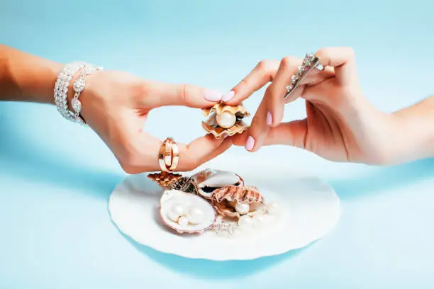Photo of beautiful woman hands with pink manicure holding plate with pearls and sea shells, luxury jewelry concept