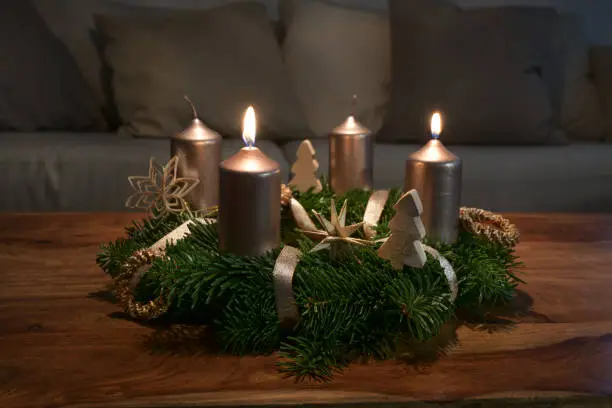 Photo of Two golden candles are lit for the second Sunday on an Advent wreath wth natural Christmas decoration on a wooden coffee table, copy space, selected focus