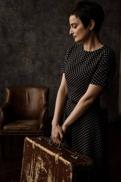 une femme brune en robe à pois tient une valise en cuir à l’ancienne, de style rétro. - polka dot suitcase retro revival women photos et images de collection